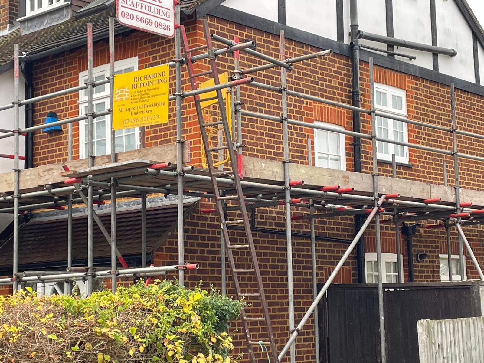 Scaffolded red brick Tudor-style house in Hampton with Richmond Repointing site board